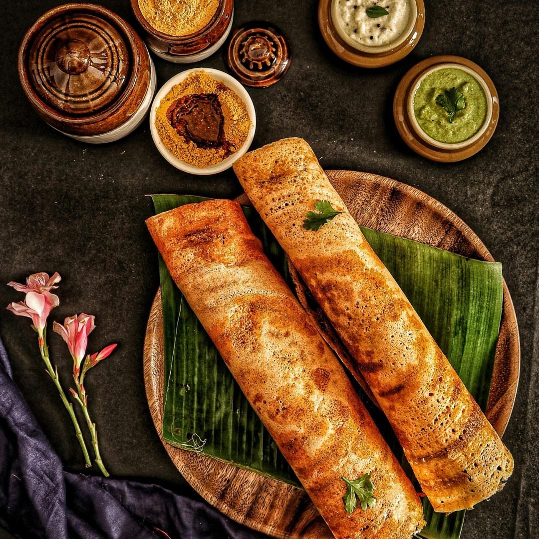 Delicious traditional dosa served with a variety of Indian chutneys and sambar on banana leaves.